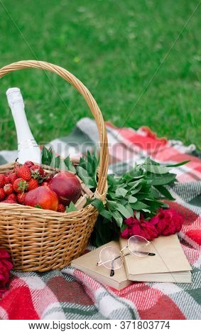 On The Grass There Is A Checkered Plaid And On It Is A Basket With Strawberries, Peaches, In The Gla