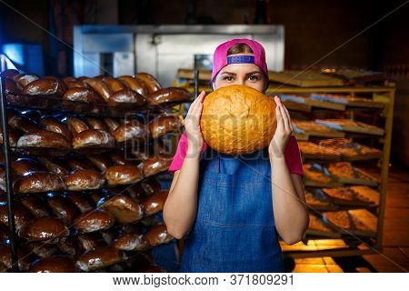 The Stage Of Baking In A Bakery. Portrait Of A Baker Girl With Bread In Her Hands Against The Backgr