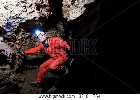Man Walking And Exploring Dark Cave With Light Headlamp Underground.