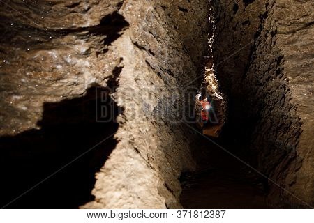 Man Walking And Exploring Dark Cave With Light Headlamp Underground.