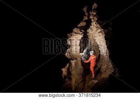 Man Walking And Exploring Dark Cave With Light Headlamp Underground.