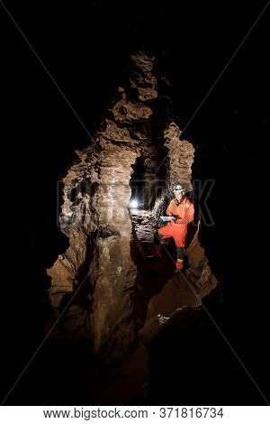 Man Walking And Exploring Dark Cave With Light Headlamp And Map In His Hand Underground.