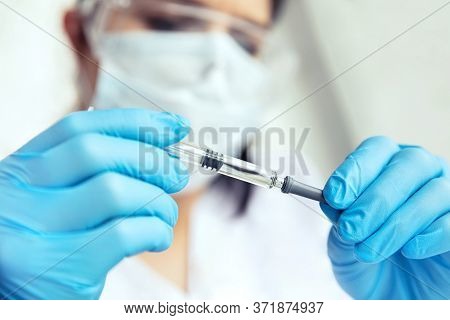Hands In Medical Gloves Holds A Syringe. Female Doctor In Protecive Glasses, Face Mask And Gloves Ho