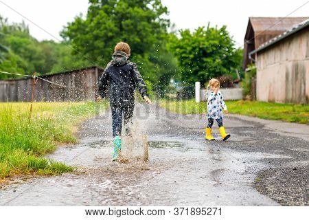 Two Children, Toddler Girl And Kid Boy Wearing Red And Yellow Rain Boots, Walking During Sleet. Happ