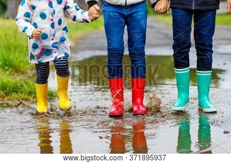 Three Children, Toddler Girl And Two Kids Boys Wearing Red, Yellow And Green Rain Boots And Walking 