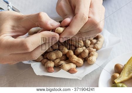 A Hand Peeling Peanuts From A Plate