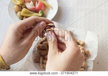 A Hand Peeling Peanuts From A Plate Next To A Olives Plate