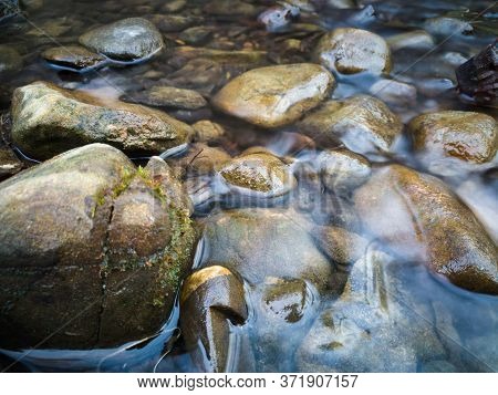 Stones Protrude From The Water In A Small Hilly Stream. The Water Murmurs Softly Between The Rocks.