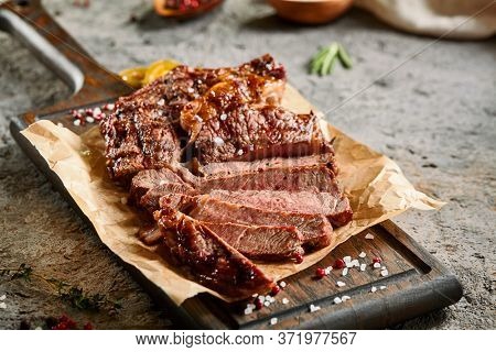 Classic ribeye steak served in waxed paper on wooden cutting board. Cut against grain beef steak. Roasted beef steak with yellow chilli pepper slices and salt crumbs. Rustic spoon and spice bowl