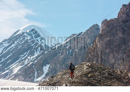 Scenic Alpine Landscape With Hiker With Trekking Poles Against Snow Mountain Peak And Sharp Rocks In