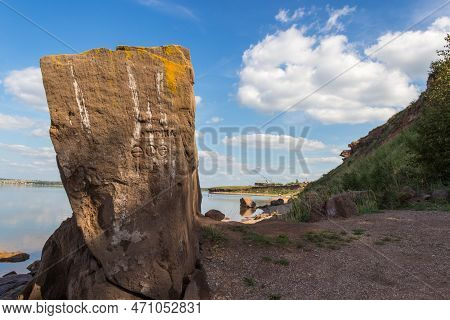 A Large Rock Sitting On The Side Of A River Or Lake