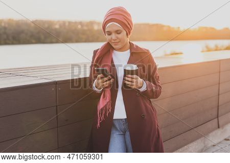 Modern Arab Girl In Hijab Walking By Street And Drinking Coffee Take Away In Spring Time Morning, Co