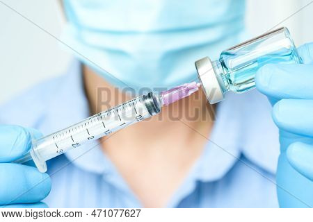 Doctor's Hand Holds A Syringe And A Blue Vaccine Bottle At The Hospital. Health And Medical Concepts