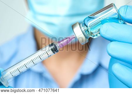 Doctor's Hand Holds A Syringe And A Blue Vaccine Bottle At The Hospital. Health And Medical Concepts