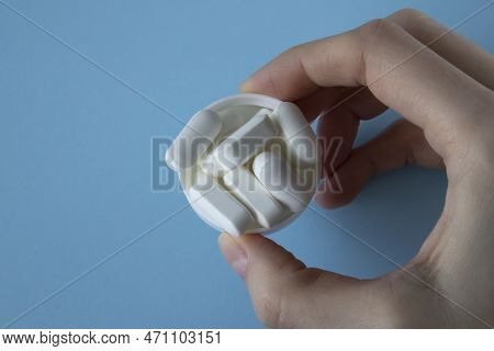 Magnesium Tablets. White Tablets With Rounded Edges In A Lid In A Womans Hand On A Blue Background.