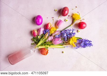 Fresh Spring Flowers In A Glass Vase With Colorful Easter Eggs On Tender Pink Background. Top View F