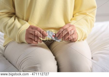 Woman Holding Blister Of Emergency Contraception Pills In Bedroom, Closeup
