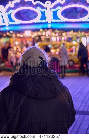 Rear Of An Old Woman With Gray Hair With A Headscarf In Front Of A Colorfully Illuminated Childrens 
