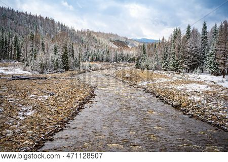 The Not Frozen Bed Of A Beautiful Winding Chibit River Flowing Through A Snow-covered Valley Surroun