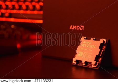 A Close-up Of An Amd Ryzen 9 7900X Processor In A Packaging Box With Backlit Keyboards In The Backgr