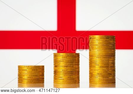Money Coins Stacks In Rising Order In Front Of England Flag. Development Of Economy Of England Conce