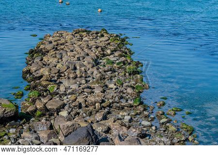 Peninsula Of Rocks Jutting Out Into Blue Ocean Water.