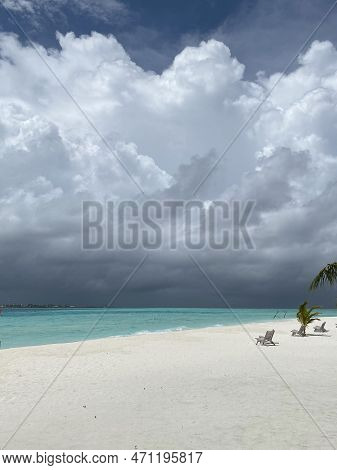 Empty White Sand Beach With Empty Beach Lounge Chairs, Clear Blue Water And Intense Cloudy Sky With 
