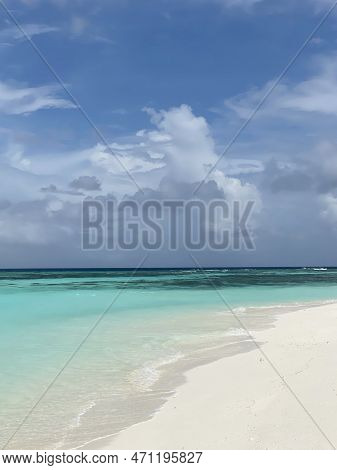 Deserted Beach With White Sand, Clean Blue Water With Coral Reef On A Sunny, Partly Cloudy Day With 