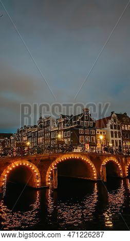 Amsterdam Bridges And Canals At Night. City View Of Amsterdam With Dutch Houses In Netherlands. Vert