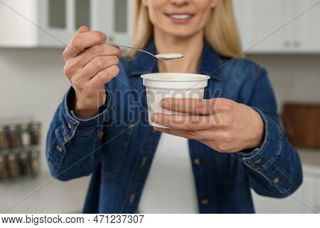 Woman Holding Plastic Cup And Spoon With Tasty Yogurt In Kitchen, Closeup