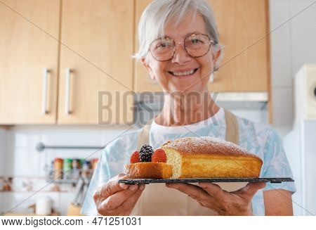 Blurred Senior Woman Looking At Camera Holding Her Freshly Baked Homemade Plumcake Served With Berri