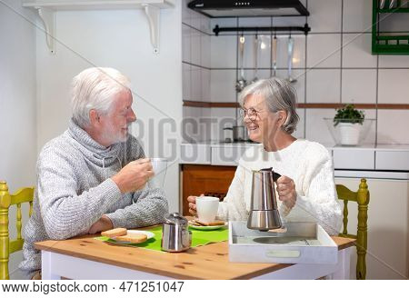 Smiling Senior Couple Having Breakfast Together At The Table At Home. Elderly Wife Holding A Coffee-