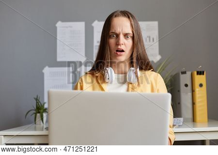 Horizontal Shot Of Shocked Scared Caucasian Woman With Brown Hair Working On Laptop In Office, Sitti