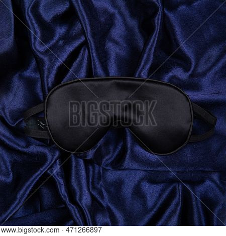 Black Silk Sleep Mask Lie On Dark Blue Silken Background. Top View. Square Orientation