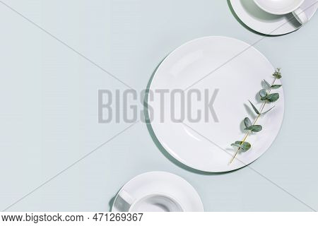 Clean, Empty White Dishes And Cups With Eucalyptus Twig On Blue Background. Eco Friendly Washing Dis