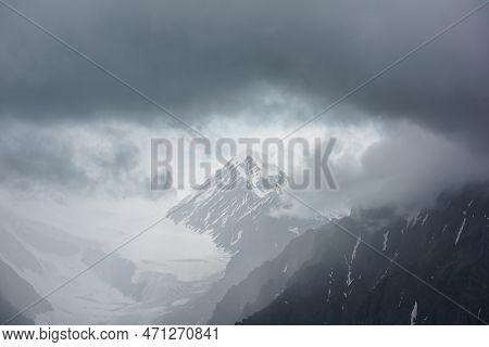 Atmospheric Landscape With Fuzzy Silhouettes Of Sharp Rocks And Snowy Mountain Top In Low Clouds Dur