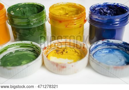 Jars Of Watercolor Paint Stand In A Row. Color Watercolor With Open Lids On A White Background. A Nu