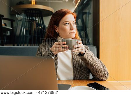 Thoughtful Woman With Ginger Hair Holding A Cup Of Coffee Sitting In A Cafe Looking At Window