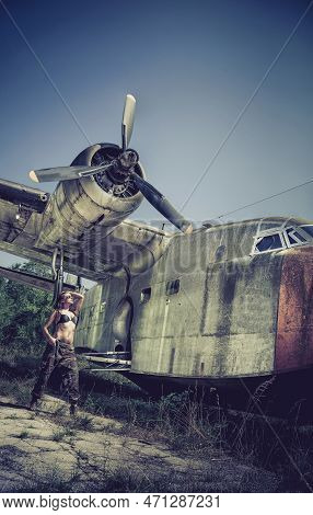 Portrait Of A Young Girl With Mimetic Military Dress Near The Old Abandoned Broken Plane. Concept Mi