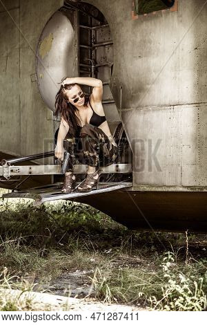 Portrait Of A Young Girl With Mimetic Military Dress Near The Old Abandoned Broken Plane. Concept Mi