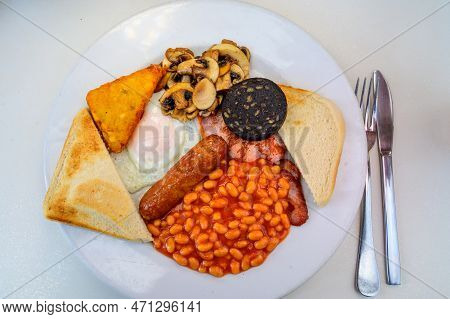White Board With Full English Breakfast With Bacon, Fried Egg, Beans, Tomato, Roasted Sausage, Black