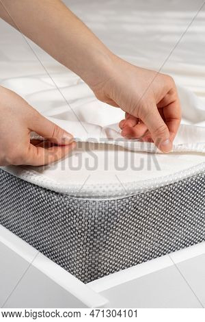 A White Satin Sheet With An Elastic Band Is Put On The Mattress Of The Bed, A Close-up Of The Hands.