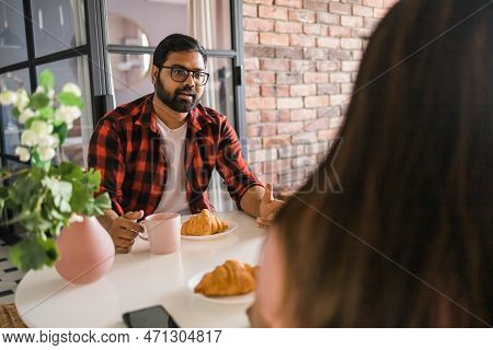 Young Diverse Loving Couple Eating Croissant And Talks Together At Home In Breakfast Time. Communica