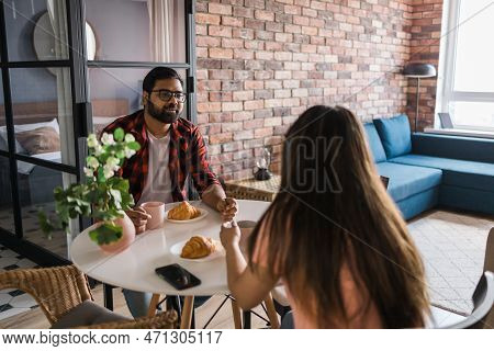 Young Diverse Loving Couple Eating Croissant And Talks Together At Home In Breakfast Time. Communica