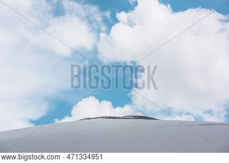 Beautiful Landscape With Huge Snowy Mountain Dome With Rocky Top Under Big Lush White Clouds In Blue
