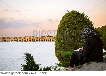 Isfahan, Iran - May 2022: Muslim Student Sit With Book Study Outside By Siose Pol Or Bridge Of 33 Ar