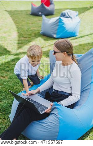 A Mother With Her Son On A Green Lawn, A Mother On Maternity Leave Is Working On A Laptop In The Par