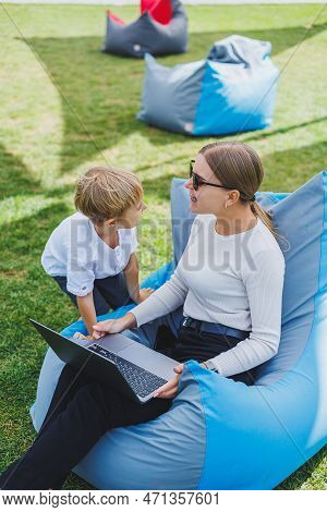 A Mother With Her Son On A Green Lawn, A Mother On Maternity Leave Is Working On A Laptop In The Par