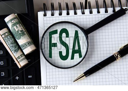 Letters Fsa (flexible Spending Account) Under A Magnifying Glass On A White Notebook Against The Bac