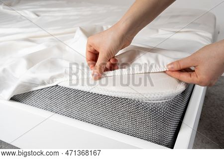 A White Satin Sheet With An Elastic Band Is Put On The Mattress Of The Bed, A Close-up Of The Hands.